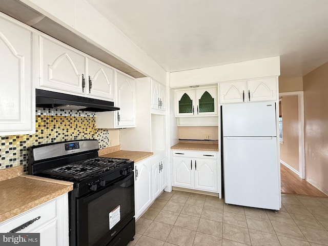 kitchen with under cabinet range hood, black gas stove, white cabinets, and freestanding refrigerator