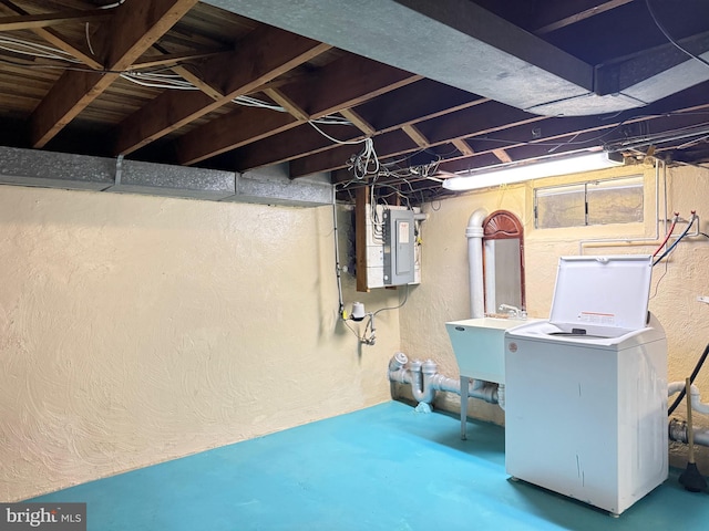 below grade area featuring electric panel, washer / dryer, a sink, and a textured wall