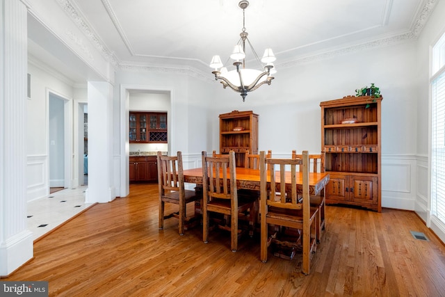 dining area featuring a chandelier, a decorative wall, light wood-type flooring, and ornamental molding