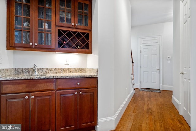 bar with a sink, indoor wet bar, baseboards, and light wood-style flooring