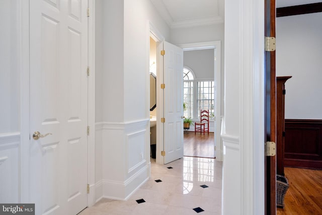 corridor with light tile patterned floors, ornamental molding, wainscoting, and a decorative wall