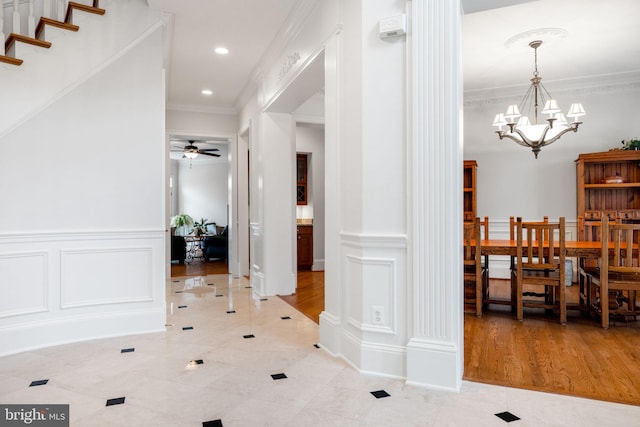 hall with a decorative wall, ornamental molding, wainscoting, and a chandelier