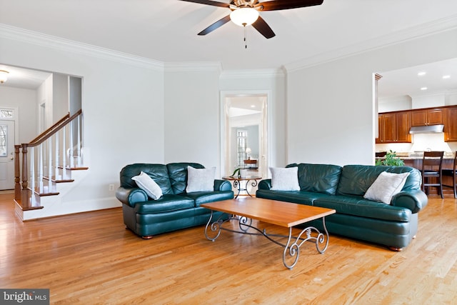 living room featuring light wood finished floors, stairs, ceiling fan, and ornamental molding