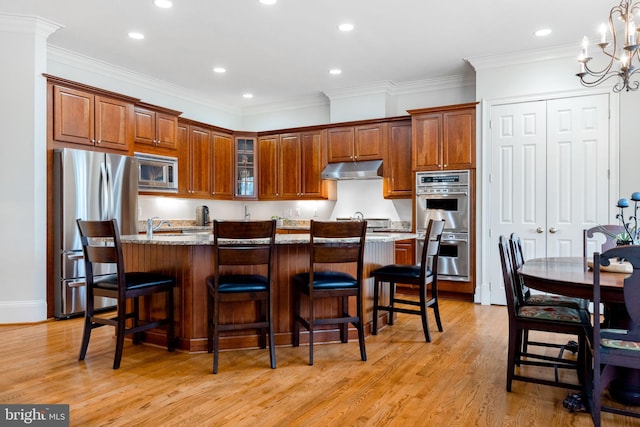 kitchen with under cabinet range hood, stainless steel appliances, crown molding, light wood finished floors, and glass insert cabinets