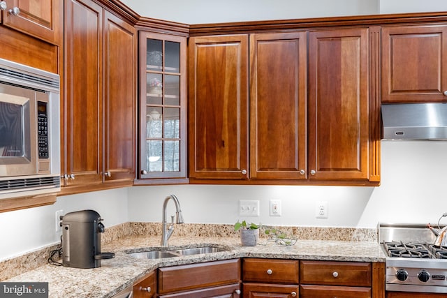 kitchen with a sink, stainless steel microwave, glass insert cabinets, and wall chimney exhaust hood