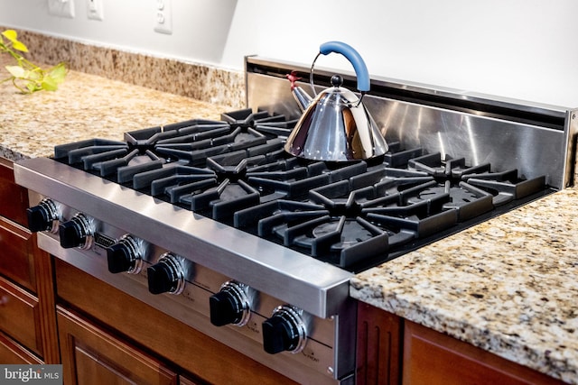 room details with range, tasteful backsplash, stainless steel gas stovetop, and light stone countertops