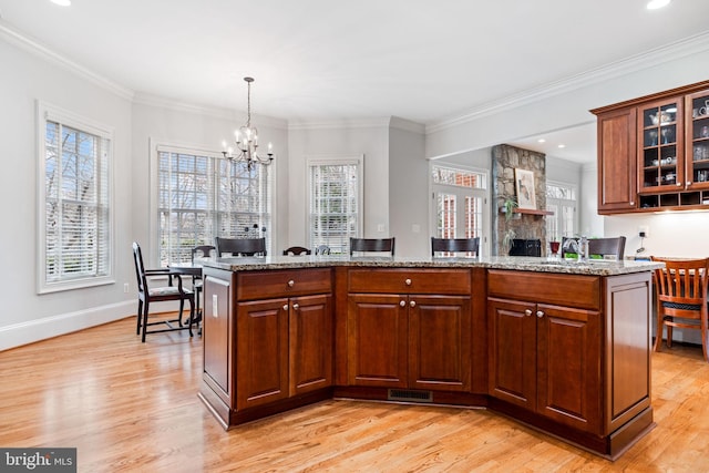 kitchen featuring light stone counters, light wood-type flooring, a chandelier, and crown molding