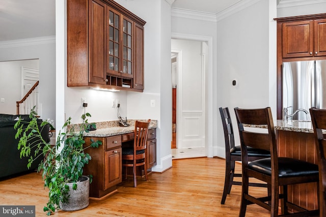 kitchen with light wood-style flooring, light stone countertops, ornamental molding, and freestanding refrigerator