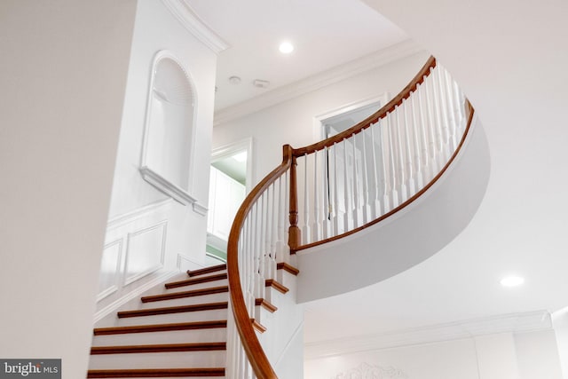 stairway featuring crown molding, a decorative wall, and recessed lighting