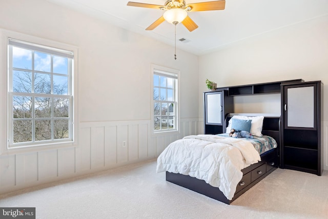 carpeted bedroom with a ceiling fan, visible vents, and a wainscoted wall