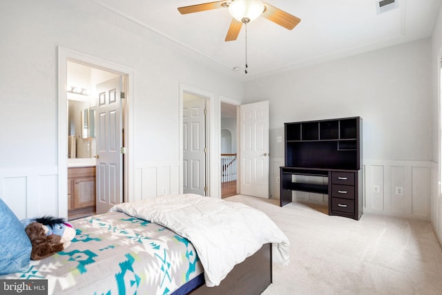 carpeted bedroom with a decorative wall, connected bathroom, visible vents, and wainscoting