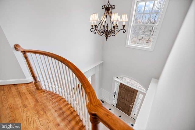 stairs featuring wood finished floors, baseboards, plenty of natural light, and a chandelier