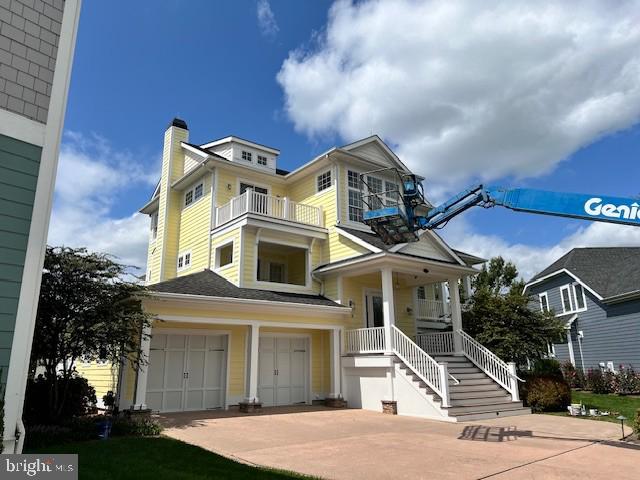 view of front of home featuring stairway, concrete driveway, a chimney, a balcony, and a garage