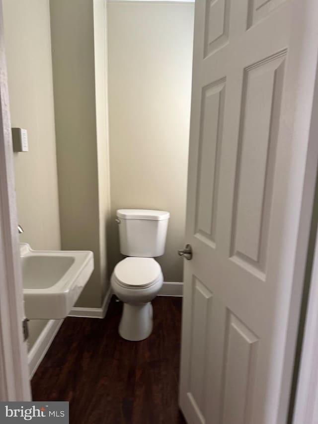 half bath featuring a sink, baseboards, toilet, and wood finished floors