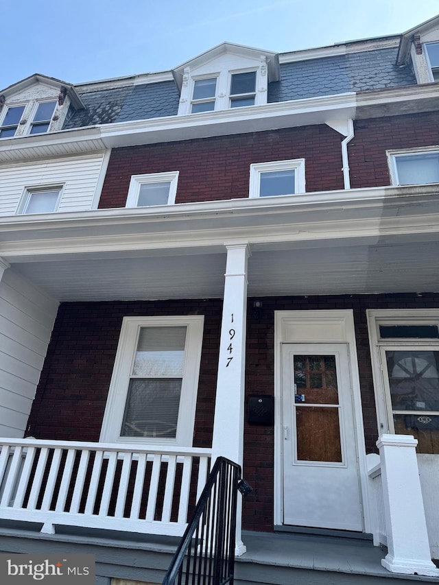 doorway to property featuring mansard roof, brick siding, and covered porch