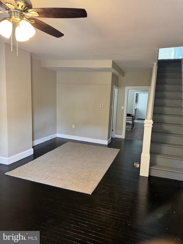 empty room featuring dark wood finished floors, baseboards, ceiling fan, and stairs