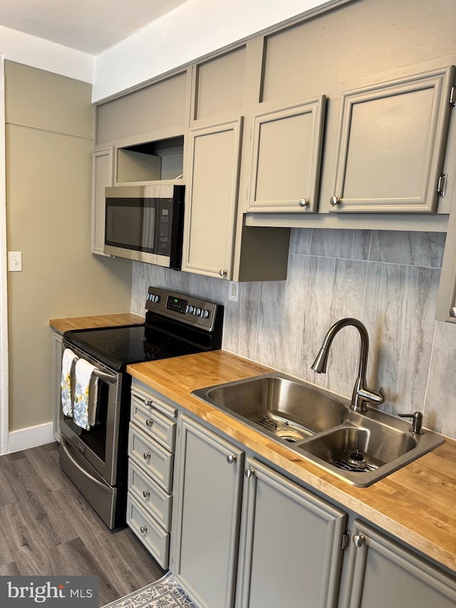 kitchen with backsplash, dark wood-style floors, stainless steel appliances, wood counters, and a sink