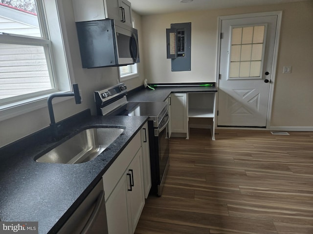 kitchen with dark wood-type flooring, electric panel, appliances with stainless steel finishes, white cabinets, and a sink