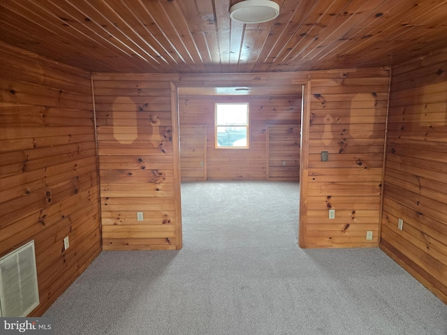 empty room featuring visible vents, carpet, wooden ceiling, and wood walls