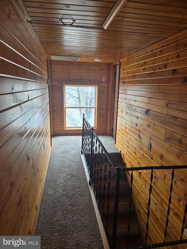 corridor featuring an upstairs landing, carpet, wood ceiling, and wooden walls