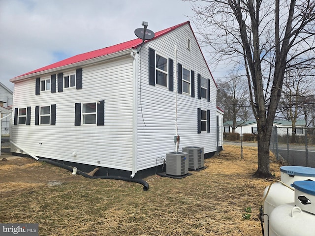 view of side of home featuring central air condition unit, metal roof, and fence