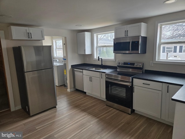 kitchen with light wood-type flooring, a sink, dark countertops, washing machine and dryer, and stainless steel appliances