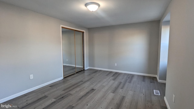 unfurnished bedroom with visible vents, wood finished floors, a closet, and baseboards