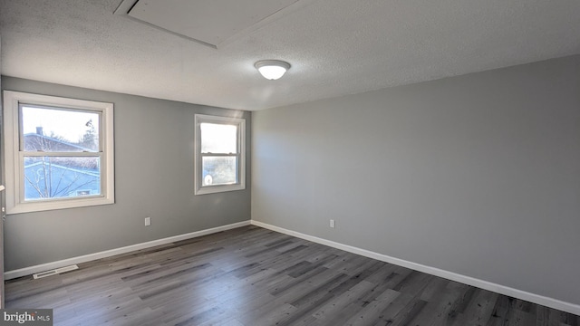 empty room featuring visible vents, a textured ceiling, baseboards, and wood finished floors