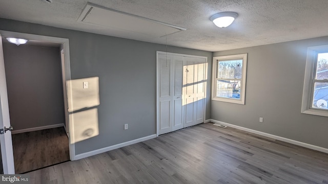 unfurnished bedroom featuring visible vents, a textured ceiling, wood finished floors, baseboards, and attic access