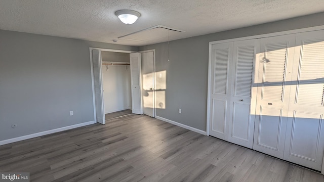 unfurnished bedroom with attic access, wood finished floors, baseboards, and a textured ceiling