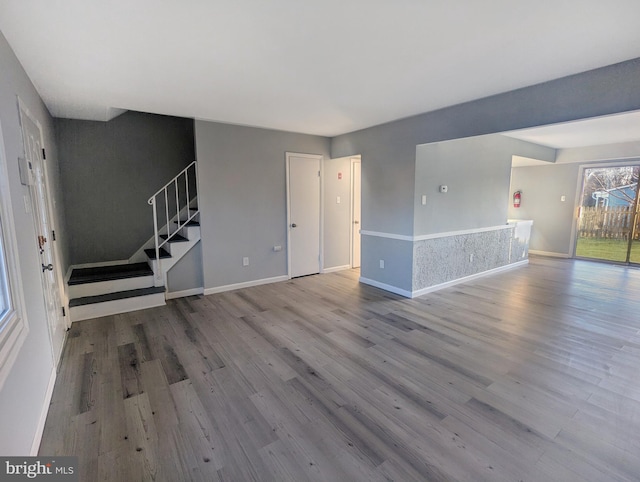 unfurnished living room with stairway, wood finished floors, and baseboards