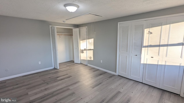 unfurnished bedroom featuring wood finished floors, baseboards, attic access, a textured ceiling, and two closets