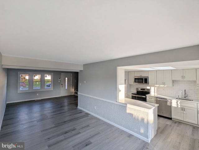 kitchen featuring a sink, backsplash, open floor plan, stainless steel appliances, and light wood finished floors