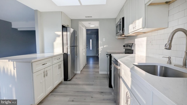 kitchen with appliances with stainless steel finishes, a skylight, light wood-style floors, white cabinets, and a sink