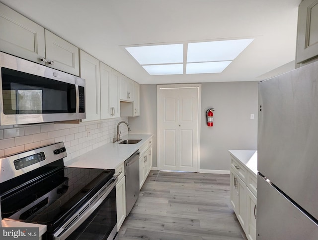 kitchen featuring tasteful backsplash, light wood finished floors, light countertops, stainless steel appliances, and a sink