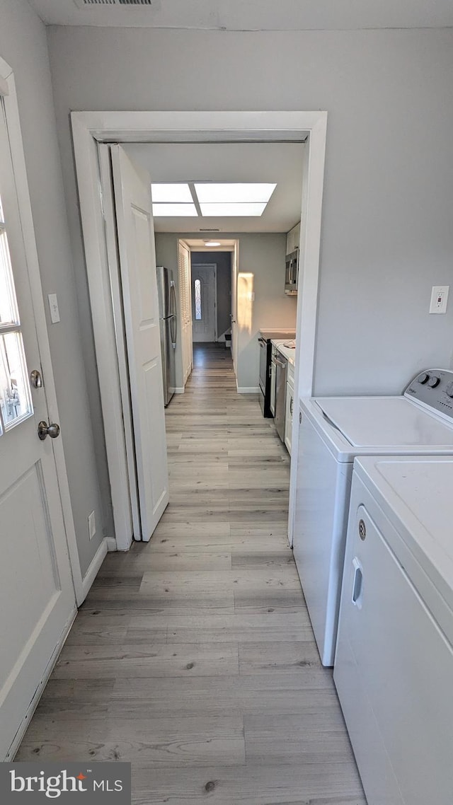 washroom featuring light wood finished floors, visible vents, baseboards, a skylight, and washer and dryer