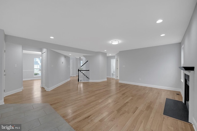 unfurnished living room featuring recessed lighting, stairway, a fireplace with flush hearth, and light wood-style floors