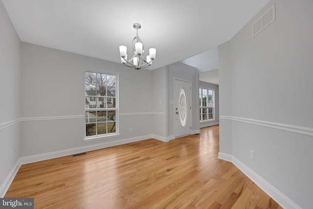 foyer featuring baseboards, visible vents, light wood finished floors, and a chandelier