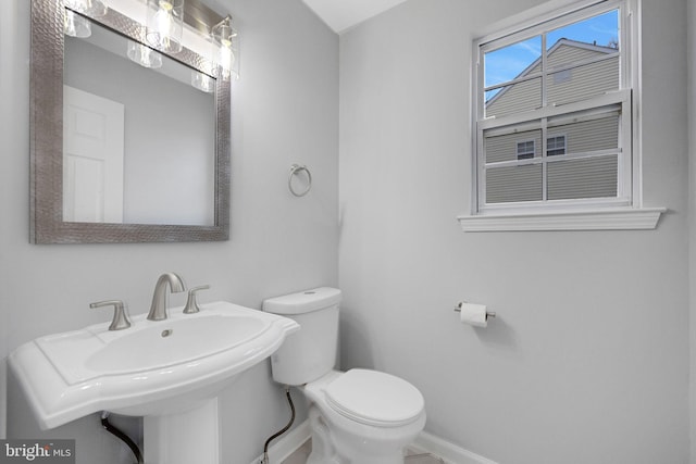 half bath featuring toilet, baseboards, and a sink