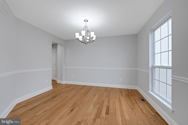 unfurnished room featuring an inviting chandelier, light wood-style floors, visible vents, and baseboards