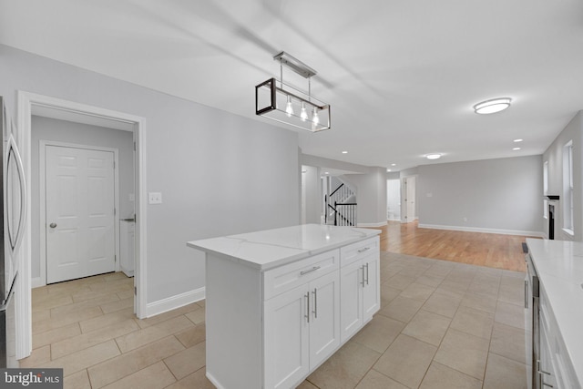 kitchen with decorative light fixtures, a kitchen island, white cabinetry, baseboards, and light stone countertops