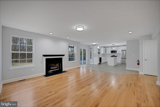 unfurnished living room with visible vents, baseboards, a fireplace with flush hearth, recessed lighting, and light wood-style flooring