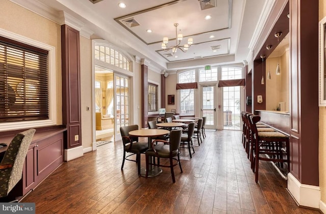 dining area featuring dark wood-style floors, visible vents, an inviting chandelier, ornamental molding, and a raised ceiling