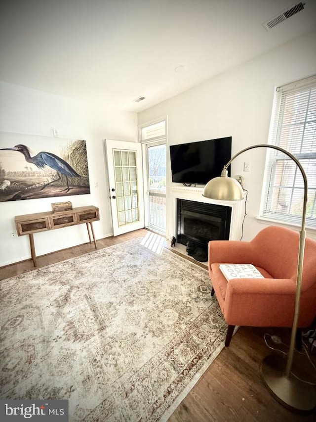 living area with a glass covered fireplace, wood finished floors, visible vents, and a healthy amount of sunlight