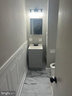 bathroom featuring vanity, a wainscoted wall, a decorative wall, toilet, and marble finish floor