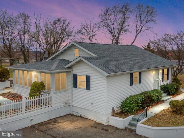 view of front of home featuring a sunroom, roof with shingles, and fence