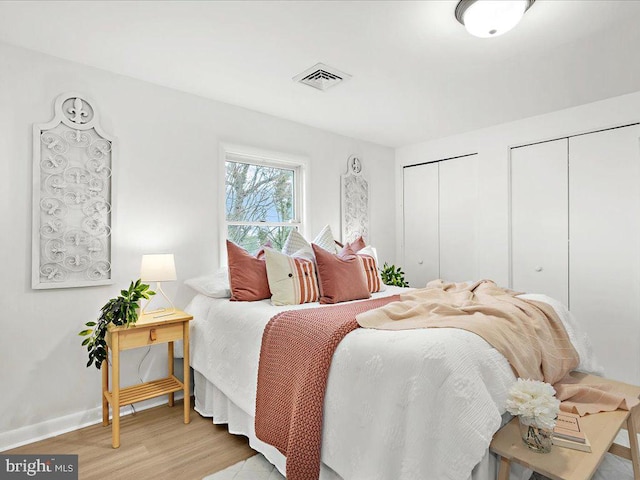 bedroom with visible vents, multiple closets, baseboards, and light wood finished floors