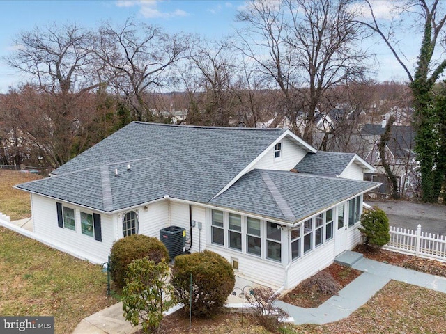 exterior space with central air condition unit, fence, a yard, roof with shingles, and a sunroom