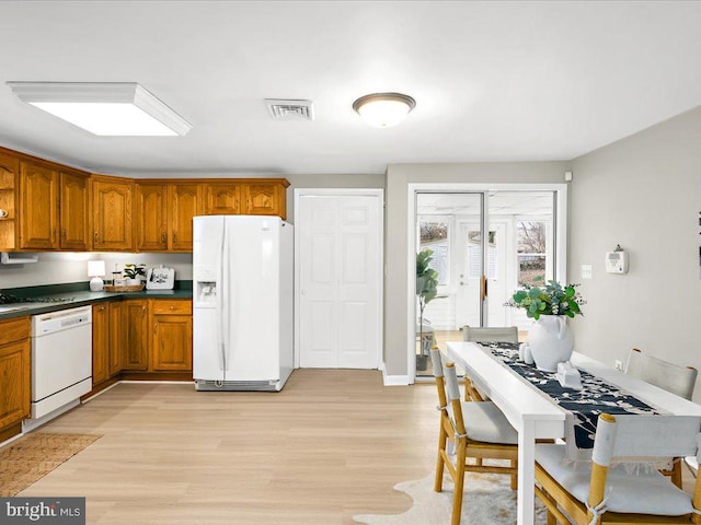 kitchen featuring brown cabinetry, light wood finished floors, white appliances, and dark countertops