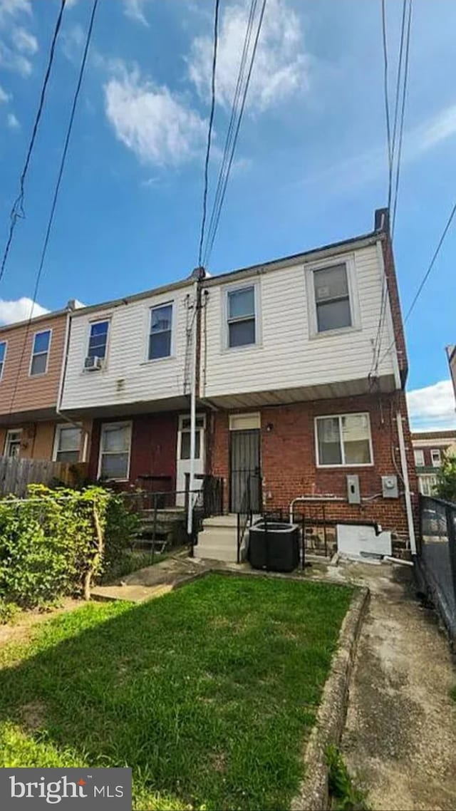back of house featuring brick siding, central AC, fence, and a lawn